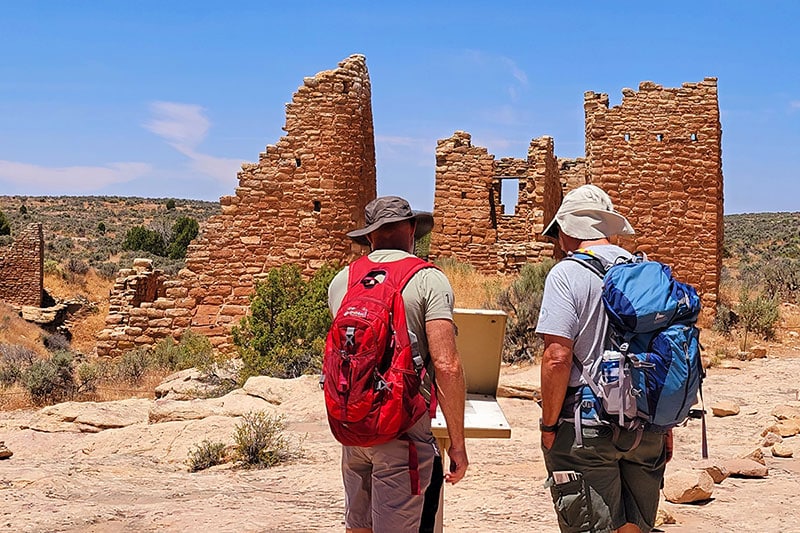 2 hikers in front of Hovenweep stone buildings